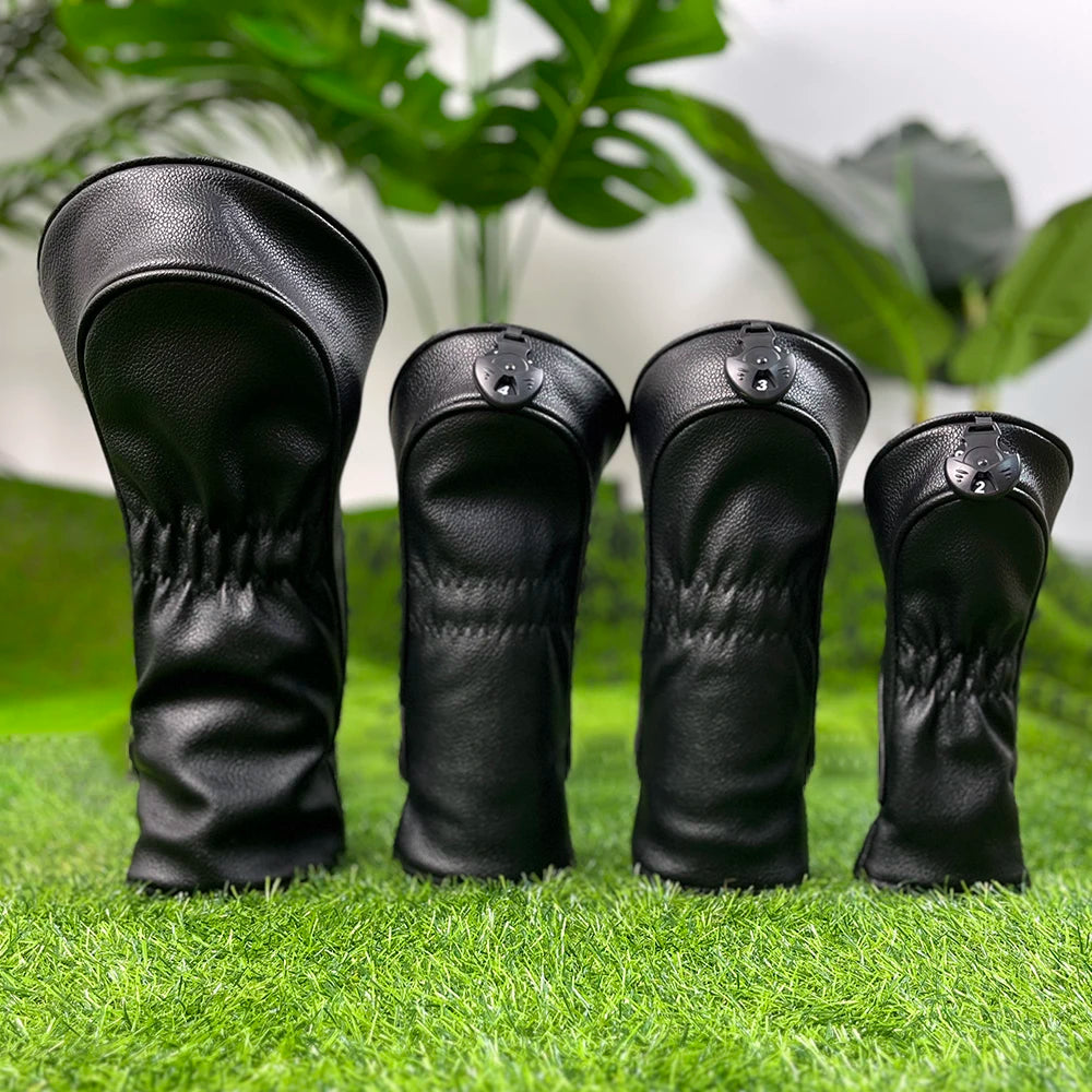 A pair of black premium wooden golf club head covers resting on green grass.