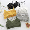 A collection of women's cross strap sports bras in black, yellow, white, and gray laid out on a white surface.