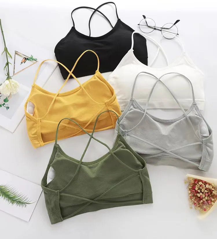 A collection of women's cross strap sports bras in black, yellow, white, and gray laid out on a white surface.