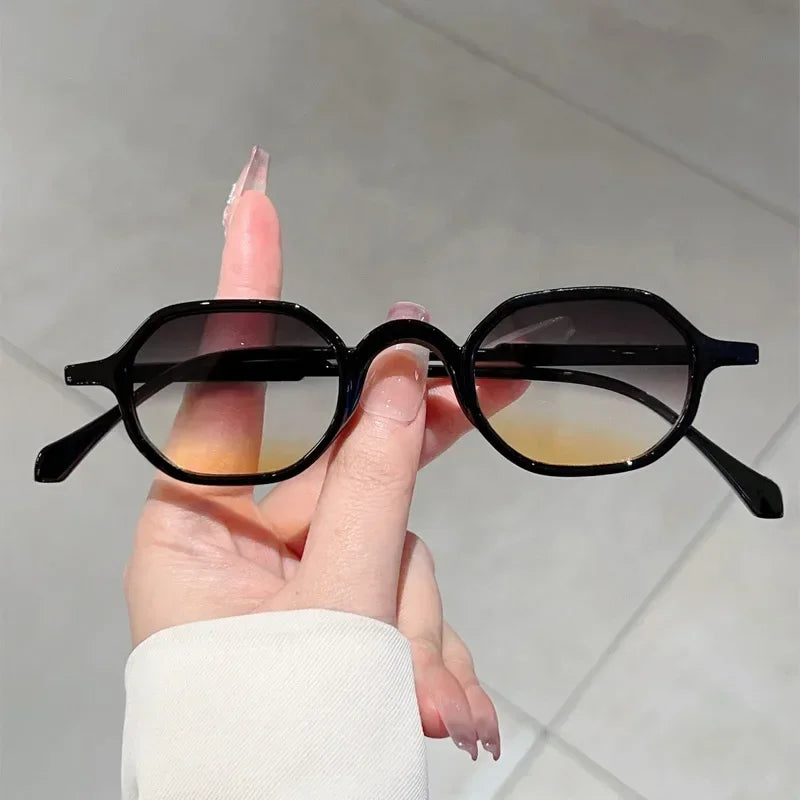 A hand holds a pair of black vintage oval sunglasses with thin frames against a light background.