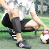 A person wearing black soccer shin guards is kneeling on a green field with a soccer ball nearby.