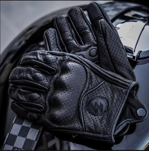 A close-up of black full finger leather motorcycle riding gloves resting on a glossy surface.