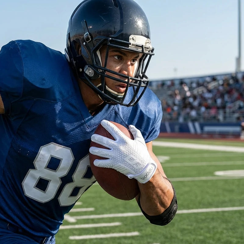 Un atleta masculino con camiseta azul y casco sostiene un balón de fútbol americano con guantes blancos sobre un fondo verde
