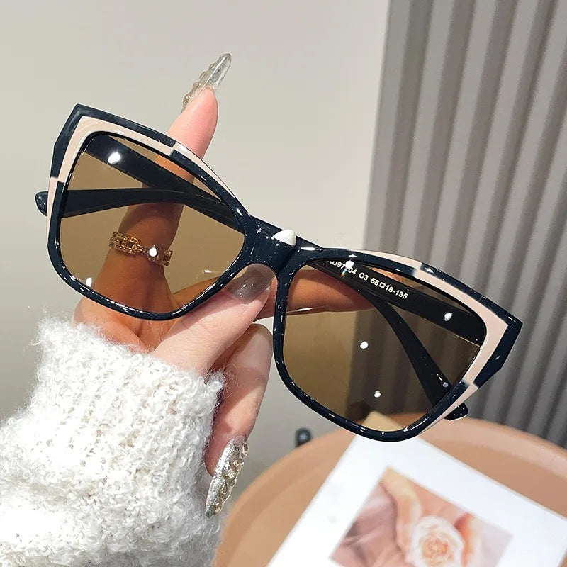 A hand holds a pair of black and beige vintage square cat eye sunglasses against a light background.