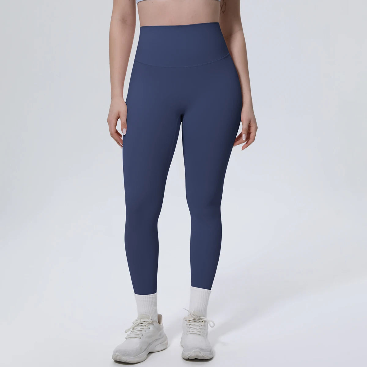 A model wearing dark blue high-waisted yoga leggings and white socks, standing against a light background.