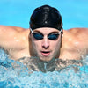 A man wearing a black silicone swim cap with blue mirrored sunglasses is submerged in water.