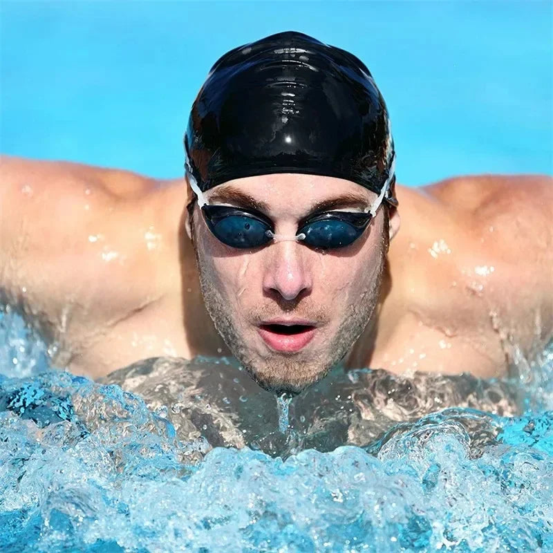 A man wearing a black silicone swim cap with blue mirrored sunglasses is submerged in water.