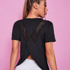 A woman wearing a black breathable summer yoga and fitness t-shirt with a sheer geometric design against a pink background.