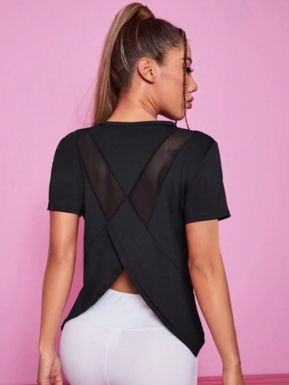 A woman wearing a black breathable summer yoga and fitness t-shirt with a sheer geometric design against a pink background.