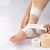 A hand is applying white athletic tape wrap to a person's ankle and lower leg.