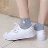 White slip-on shoes with grey ankle socks featuring a small embroidered yellow bird