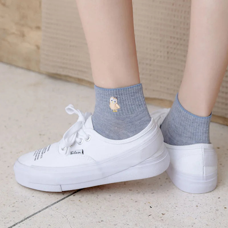 White slip-on shoes with grey ankle socks featuring a small embroidered yellow bird