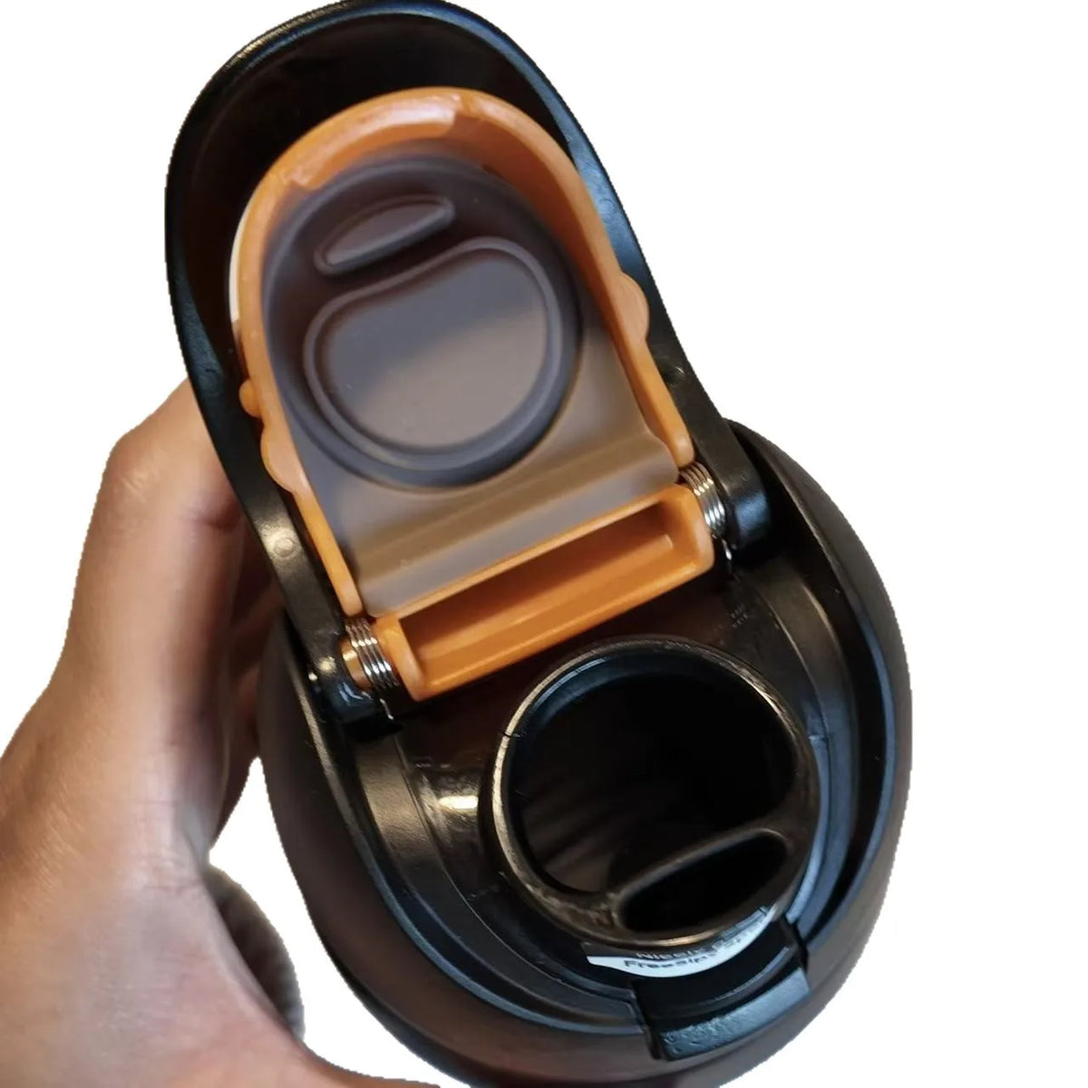 A hand holds a black vacuum insulated water bottle with an orange lid and straw opening.