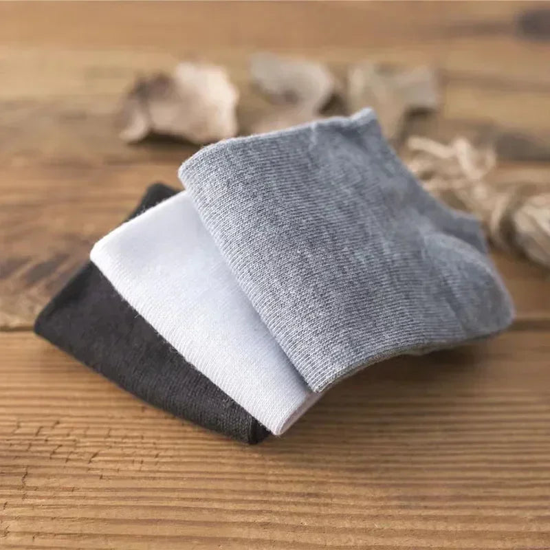 Una pila de calcetines de algodón transpirables de tobillo en gris, blanco y negro sobre una superficie de madera.