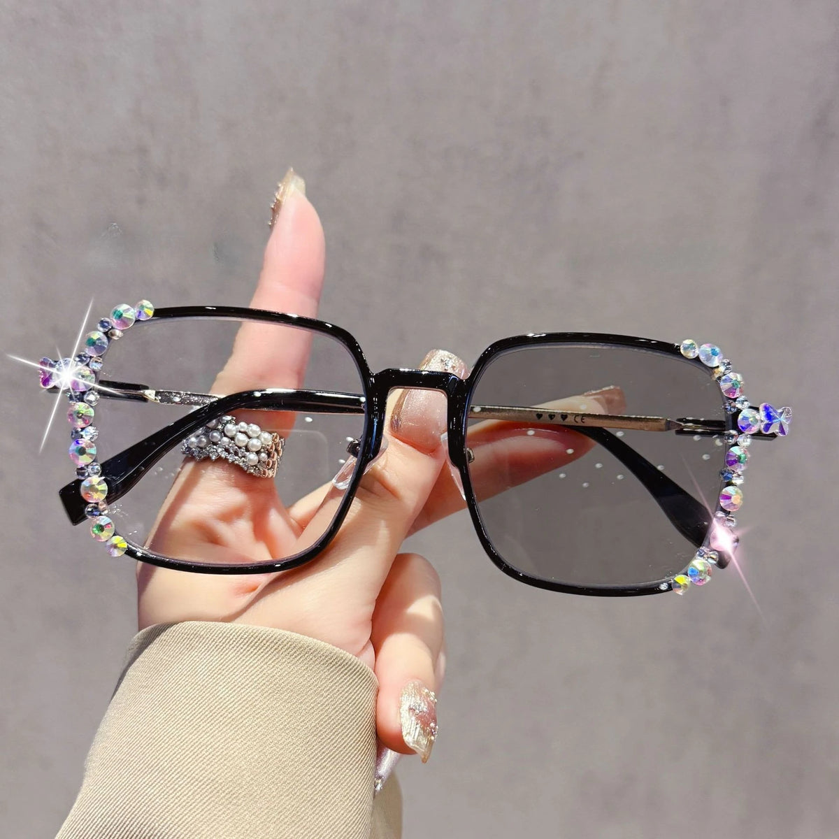 A hand holds a pair of black photochromic eyeglasses decorated with sparkling diamonds and rhinestones.