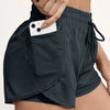 A close-up of dark gray athletic shorts with mesh pockets, showing a hand placing a smartphone into a pocket.