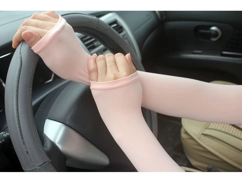 A person wearing light pink breathable arm sleeves gripping a car steering wheel.