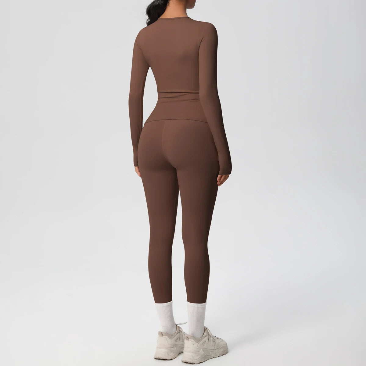 A woman wearing a long-sleeved, fitted, mocha brown performance yoga and gym set with white sneakers.