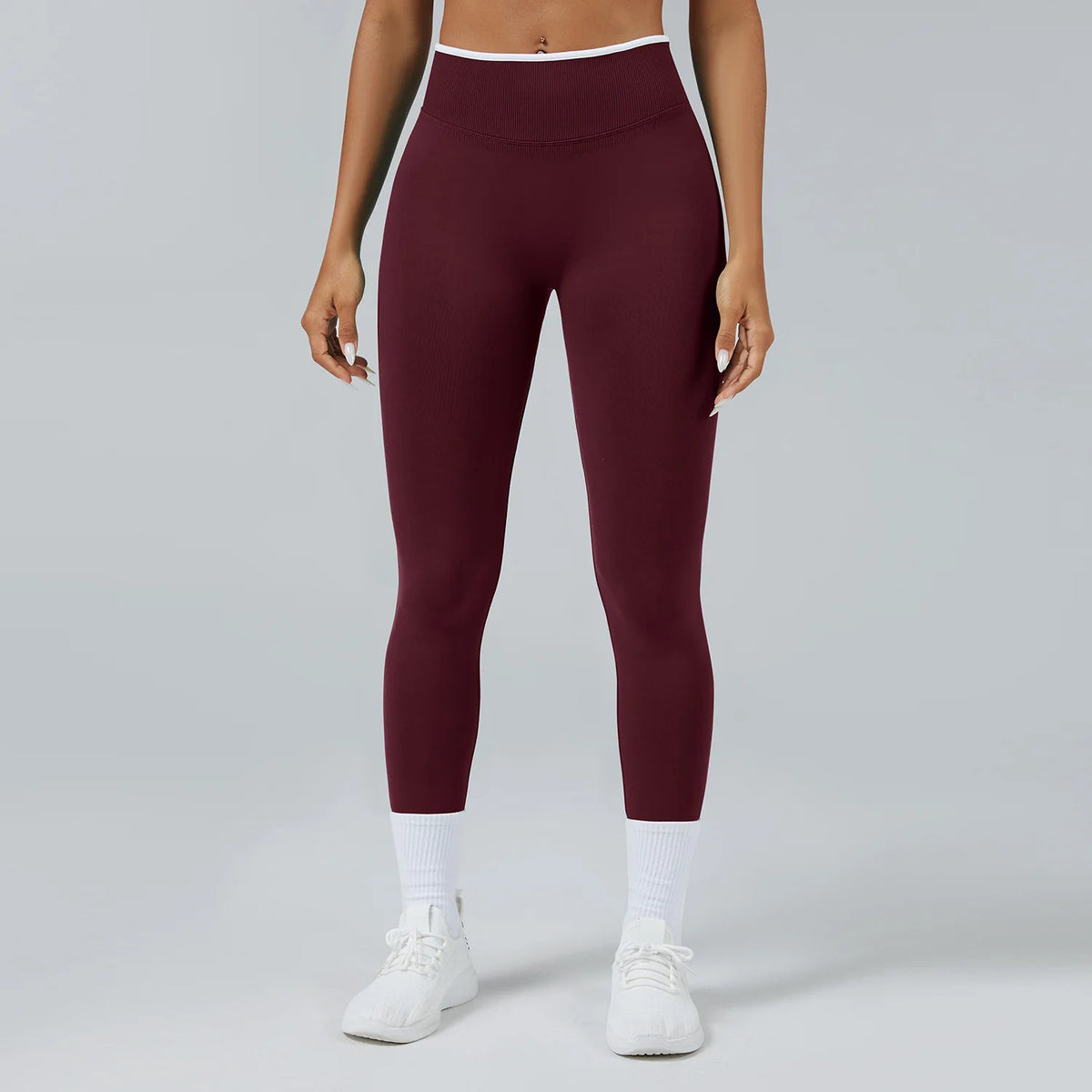 A model wearing maroon high-waist yoga leggings with white trim and white socks and white sneakers.