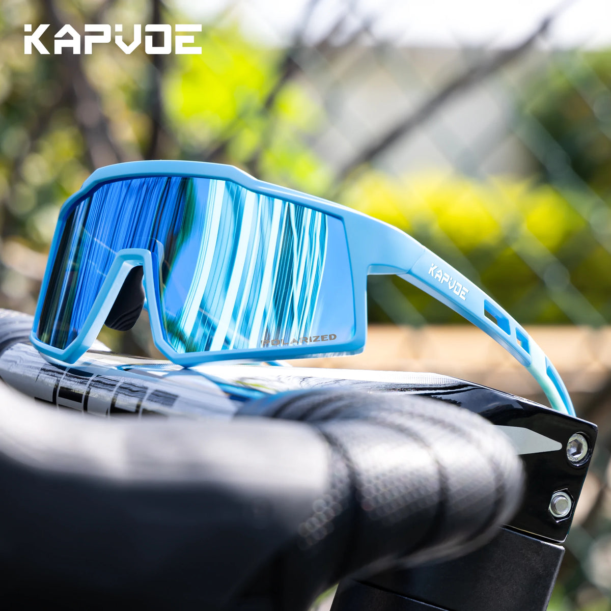 A pair of bright blue polarized sports sunglasses with a light blue frame resting on a black bicycle handlebar.