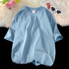 Helles blaues, oversized Baumwoll-T-Shirt für Damen, flach auf einer Oberfläche mit rosa Blumen und Sonnenbrille
