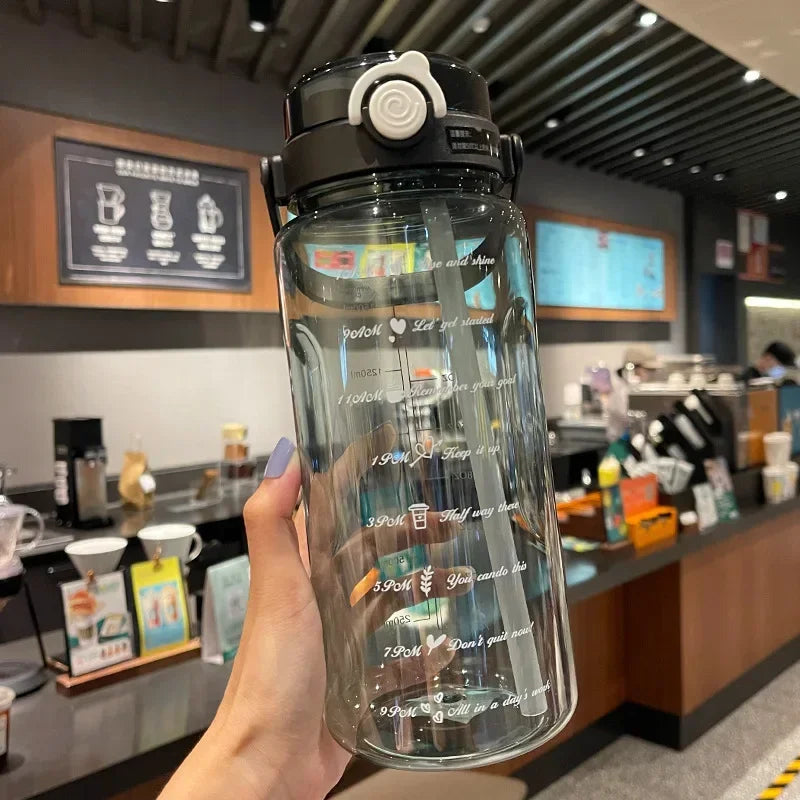 A clear sports water bottle with a time scale marked on the side is held up against a blurred background of a cafe.