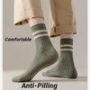 Close-up of beige trousers and a person wearing olive green striped socks with a ribbed cuff.