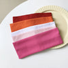 A stack of five colored elastic hairbands in shades of orange, pink, and white resting on a light plate.