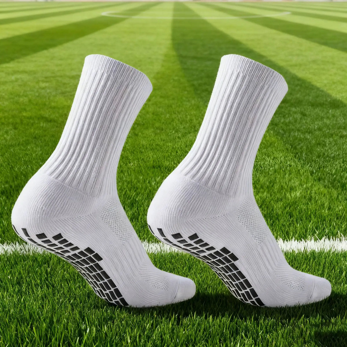 Une paire de chaussettes de football en silicone antidérapantes blanches posées sur un terrain de soccer vert.