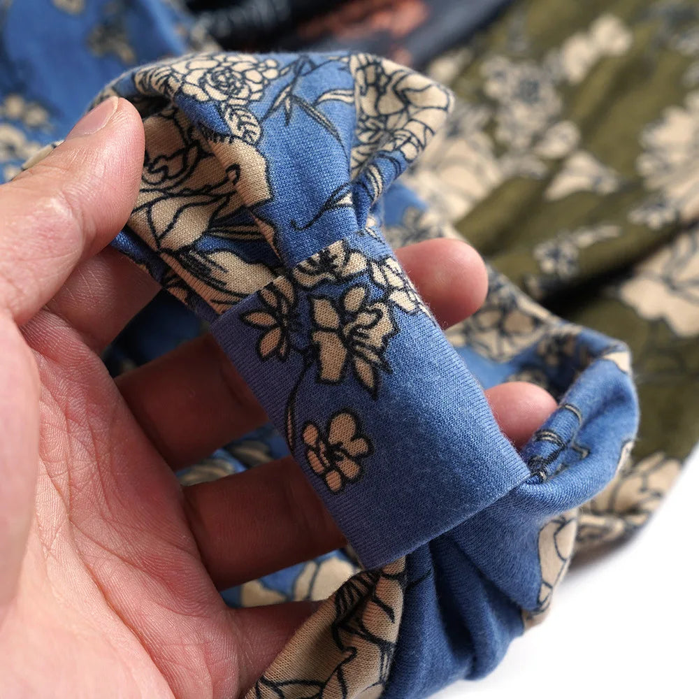 A hand is holding a blue bohemian cotton stretch headband with a floral pattern.