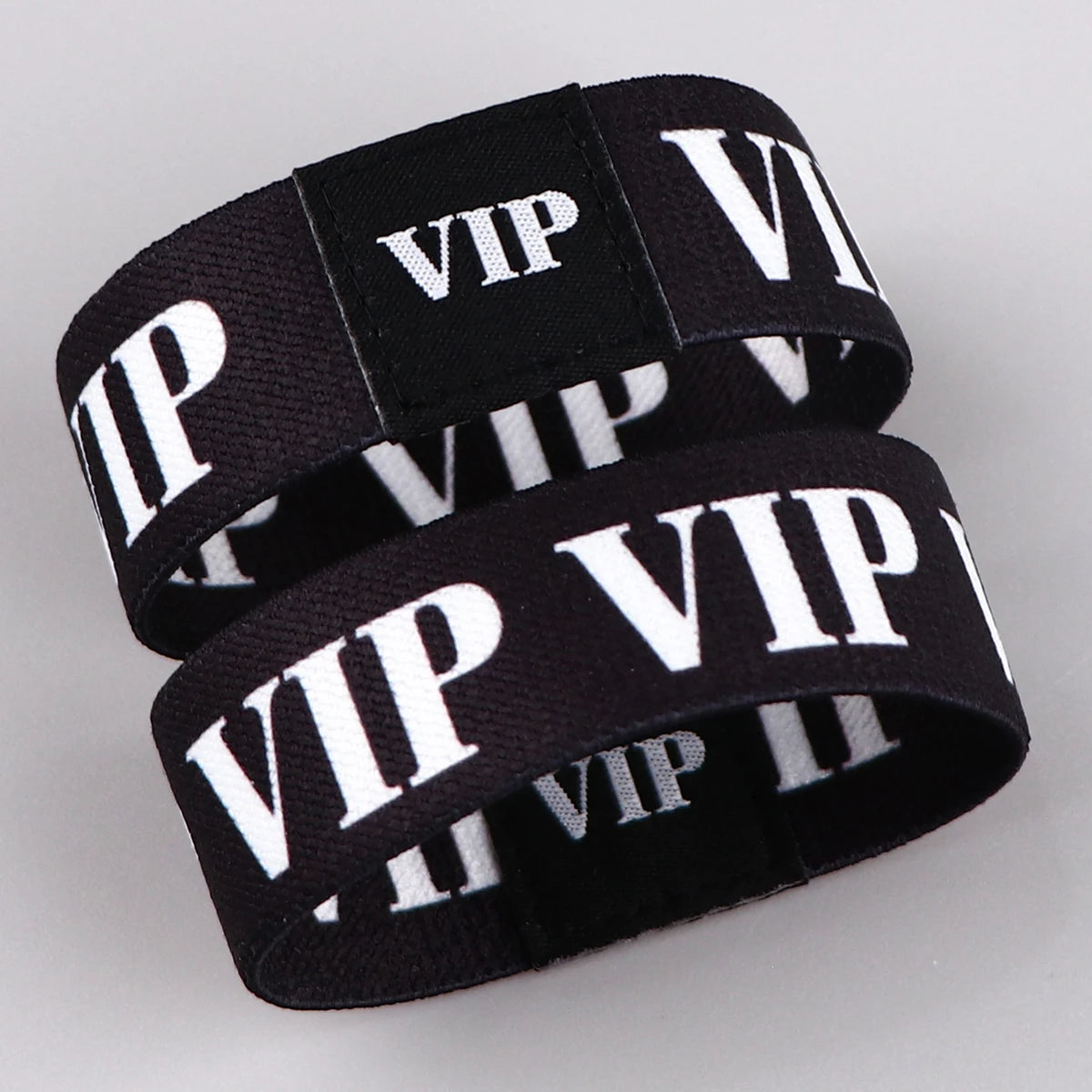 Schwarze Acryl-Elastikarmbänder mit weißer VIP-Beschriftung auf hellem grauem Hintergrund.