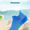 A blue and black performance compression sports sock is displayed on a sandy surface with a tropical background.