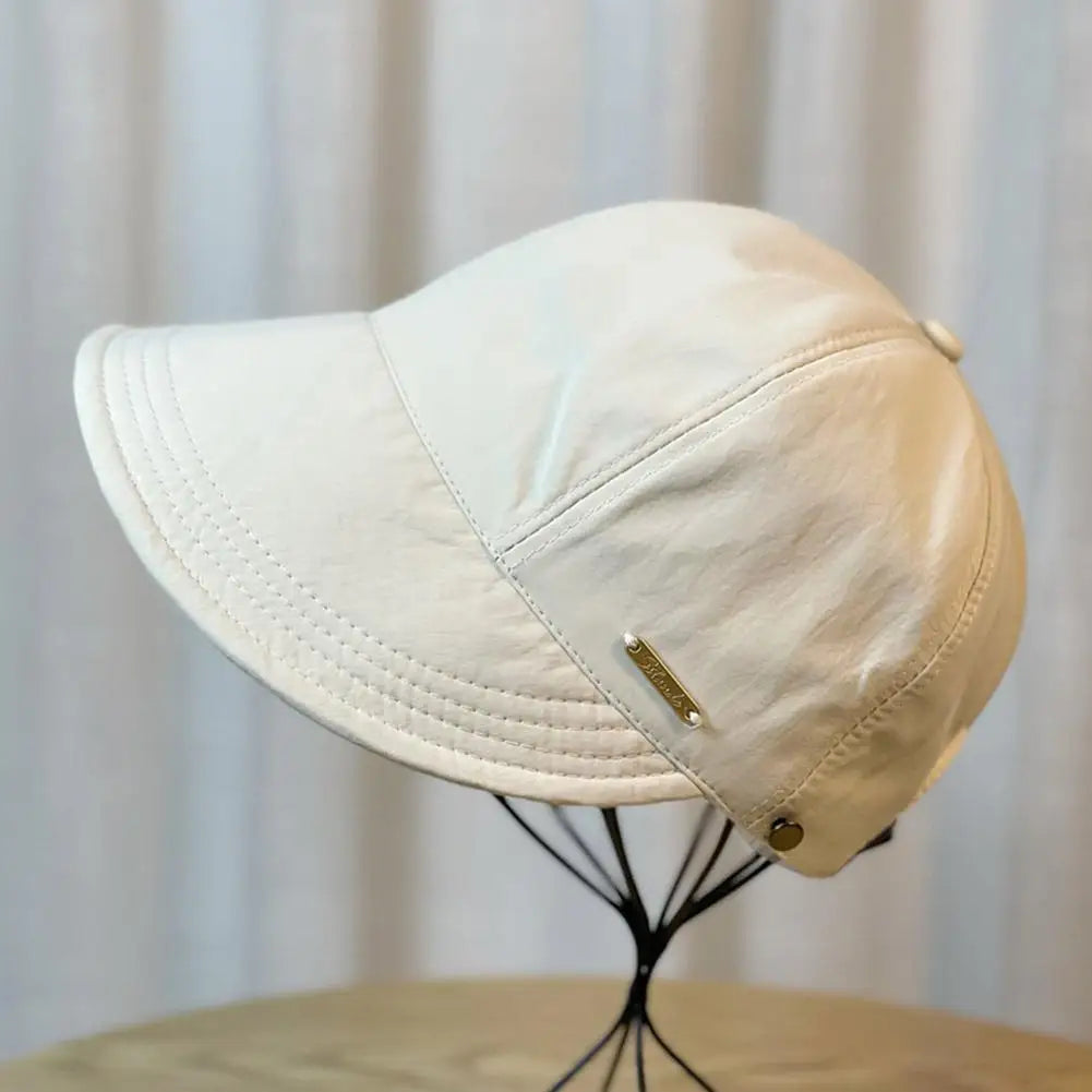 Gorra de béisbol de ala ancha y protección UV de color crema exhibida en un soporte negro.