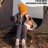 A woman wearing an orange beanie and jeans is sitting inside a tent with a dog, holding an insulated water bottle.