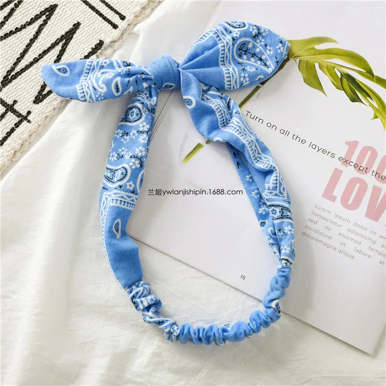Bandeau bohème à motif paisley bleu, noué avec un nœud en tissu, exposé sur du blanc et du tissu naturel.