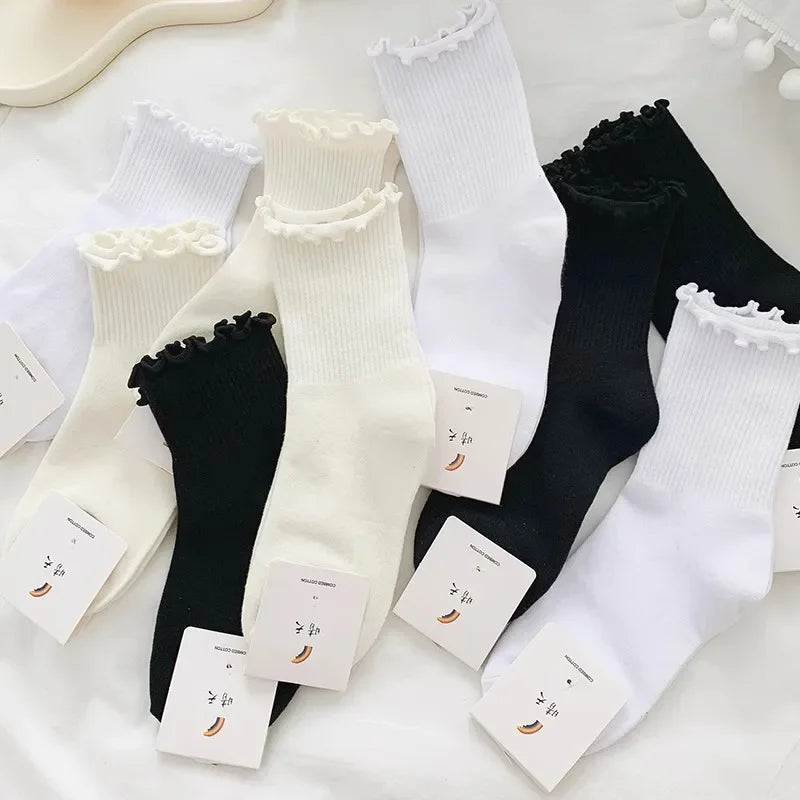 A stack of white and black cotton ruffle ankle socks displayed on a white background.