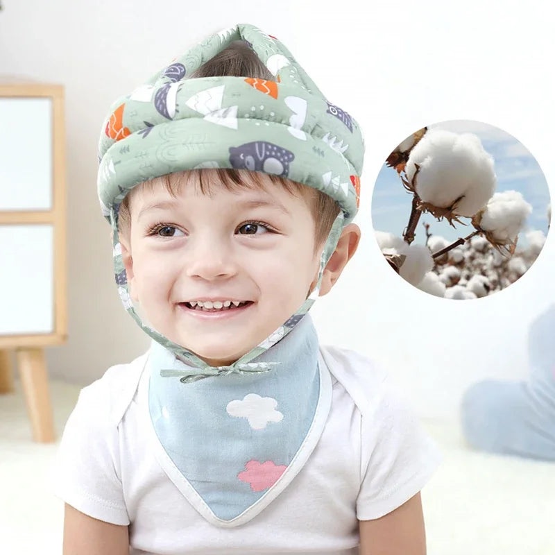 A smiling toddler wearing a soft adjustable safety helmet patterned with clouds and animals.