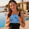 A young woman smiling while holding a blue butterfly print silicone swimming cap near a pool.