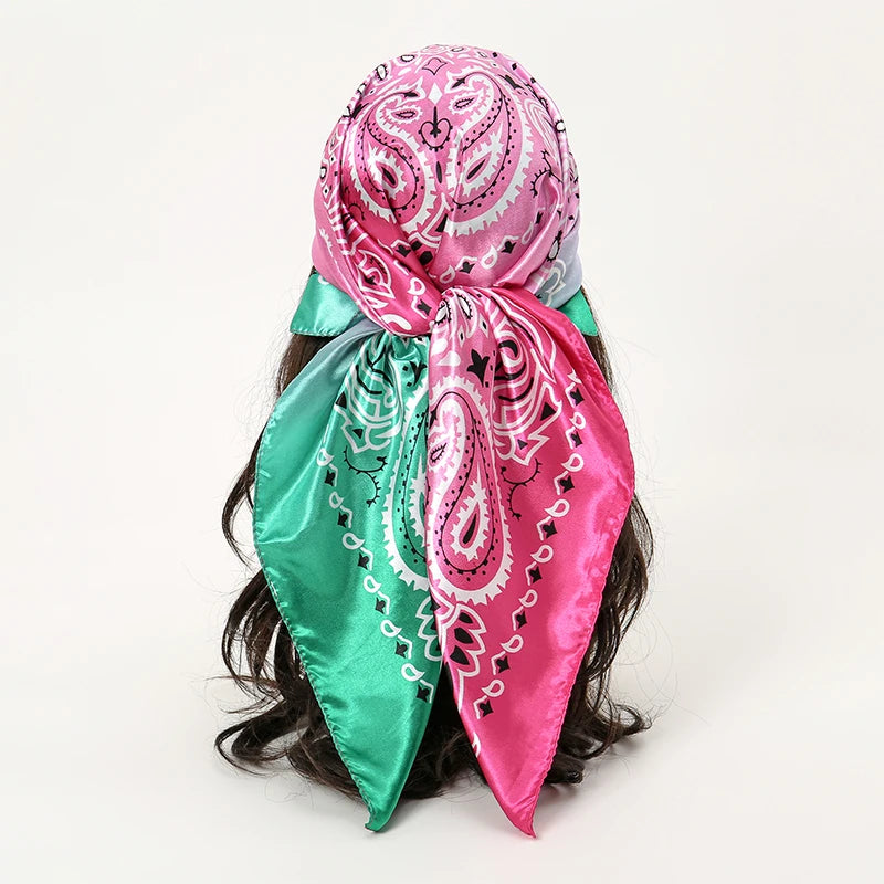 A vibrant pink and teal satin square scarf tied around dark hair.