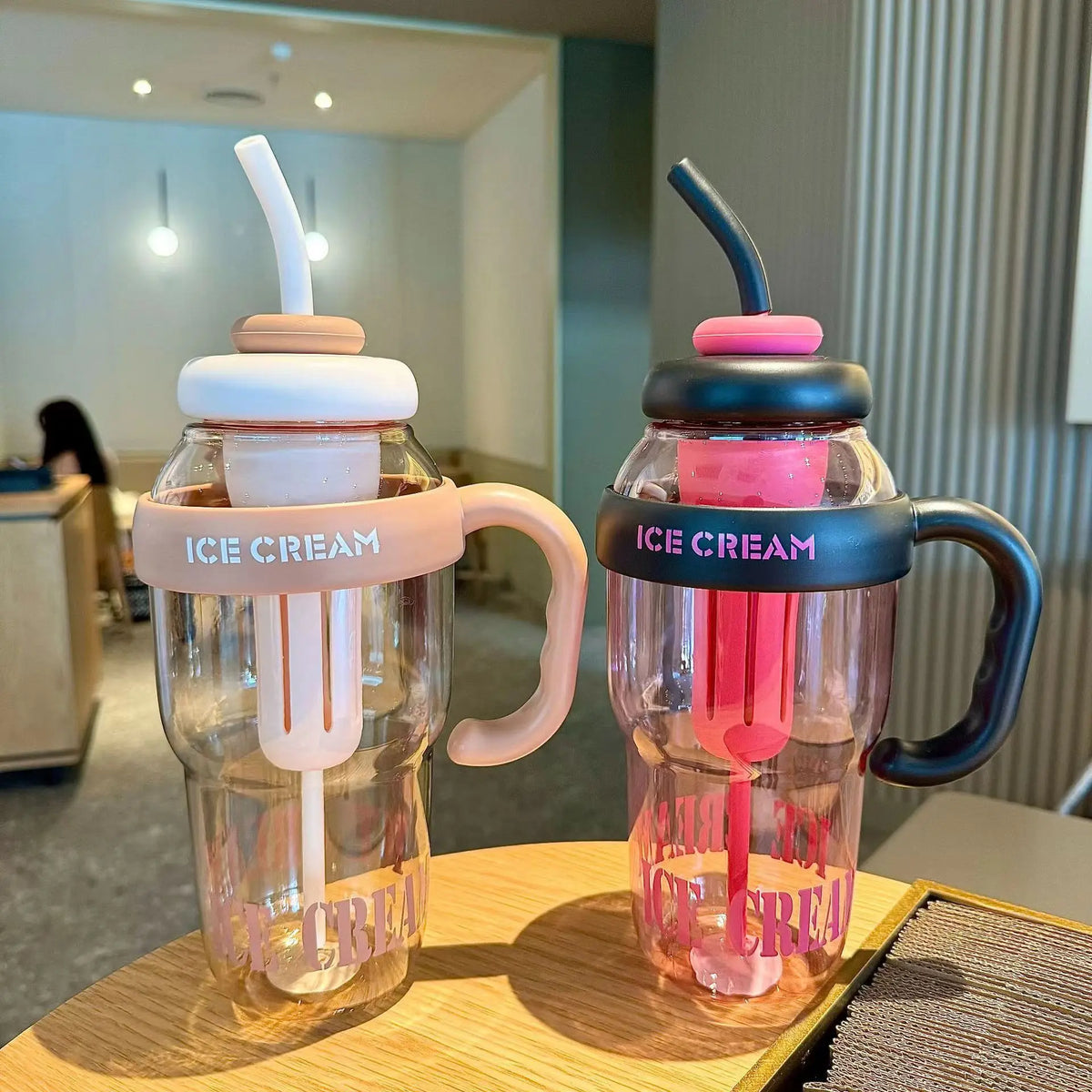 Two clear reusable water bottles with straws and handles, colored pink and dark gray, sitting on a wooden surface.