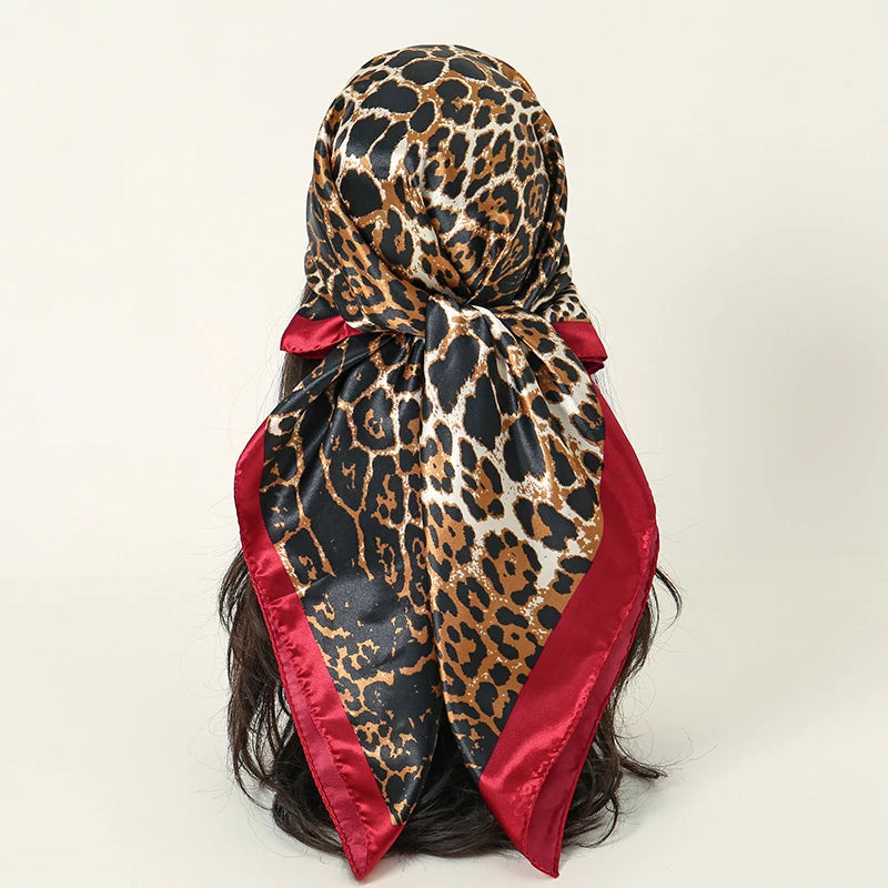 A black and gold leopard print satin square scarf tied around dark hair.