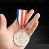 A hand holds a gold sports achievement medal with laurel wreaths and a ribbon featuring red, white, and blue stripes.