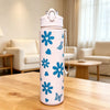 A pink reusable water bottle with blue floral and butterfly designs sits on a wooden table in a bright living room.