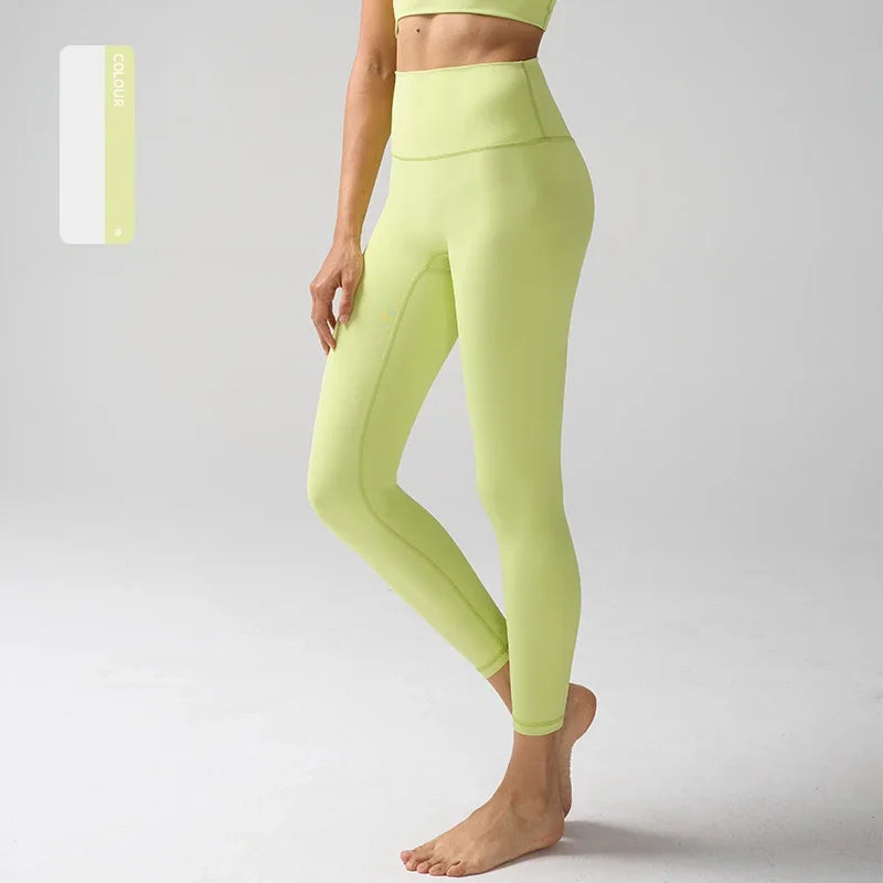 Une femme portant des leggings de performance vert lime taille haute, debout sur un fond gris clair.