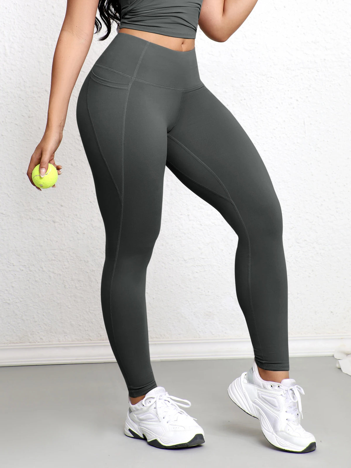 A woman wearing dark gray high-waisted sports leggings and white sneakers standing indoors.