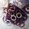 A pile of 50 mixed color elastic hair bands in various shades of purple, pink, and brown.