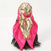 A pink satin square scarf with gold detailing tied around a dark hairstyle.