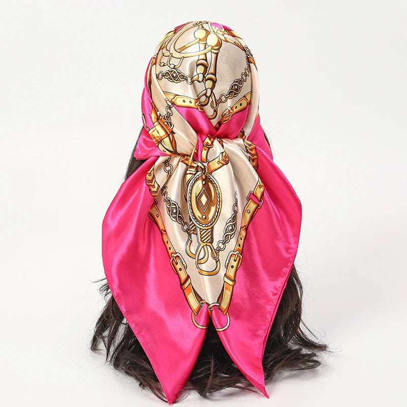 A pink satin square scarf with gold detailing tied around a dark hairstyle.