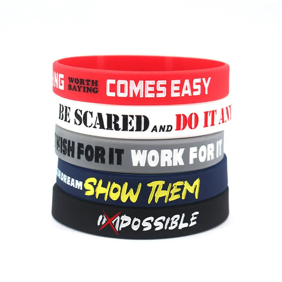 Tres pulseras de silicona apiladas con texto motivacional en bandas rojas, blancas y gris oscuro.