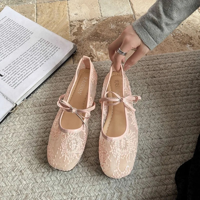 Un par de bailarinas de encaje rosa pálido sobre una superficie beige texturizada junto a un libro abierto.